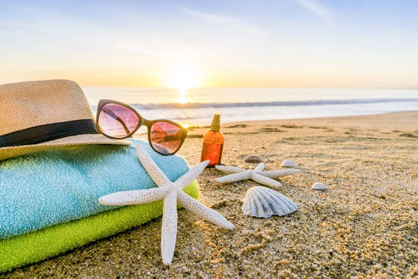 Sunglasses, towels, hat, sun block, shells and starfish on sandy