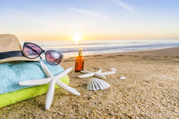 Sunglasses, towels, hat, sun block, shells and starfish on sandy