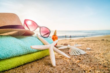 Güneş gözlüğü, havlu, şapka, güneş kremi, kabukları ve denizyıldızı sandy üzerinde