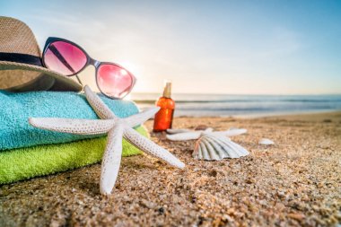 Güneş gözlüğü, havlu, şapka, güneş kremi, kabukları ve denizyıldızı sandy üzerinde