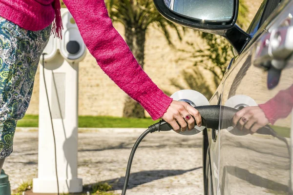 Kvinna pluggar elbilen till laddningsstationen — Stockfoto