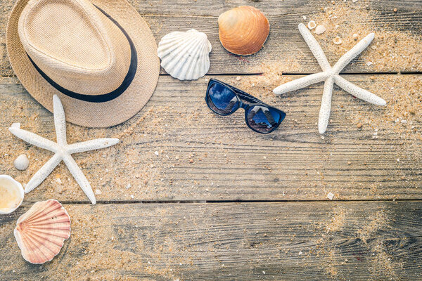 Summer hat, shells and sun glasses on wooden and sandy backgroun