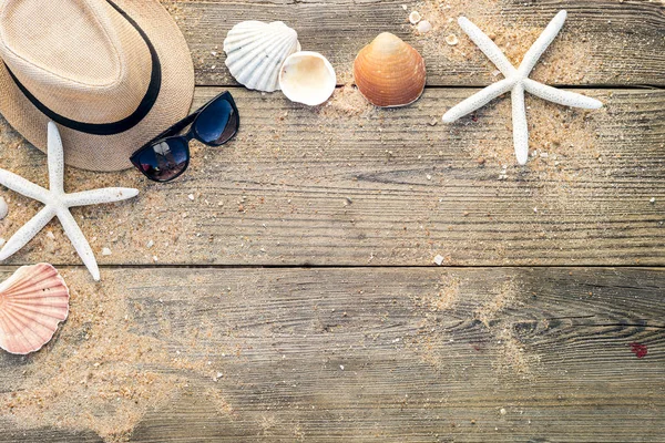 Cappello estivo, conchiglie e occhiali da sole su backgroun di legno e sabbia — Foto Stock