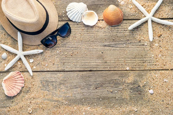 Cappello estivo, conchiglie e occhiali da sole su backgroun di legno e sabbia — Foto Stock