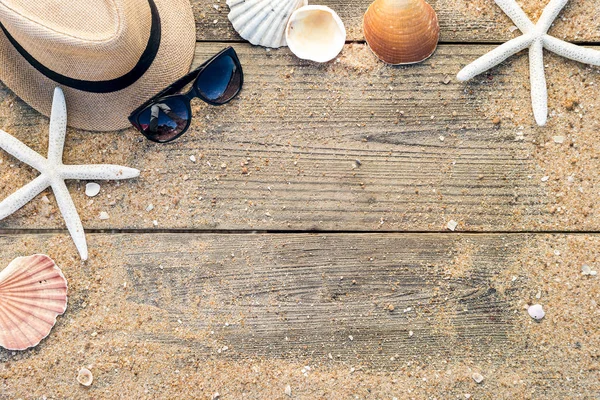 Cappello estivo, conchiglie e occhiali da sole su backgroun di legno e sabbia — Foto Stock