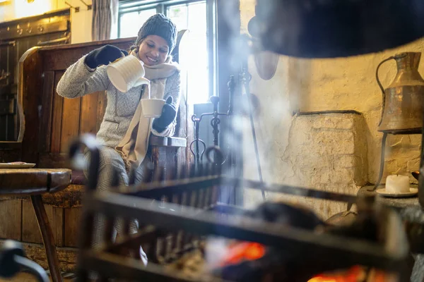 Junge schöne Frau wärmt sich mit Tee am Kamin auf — Stockfoto