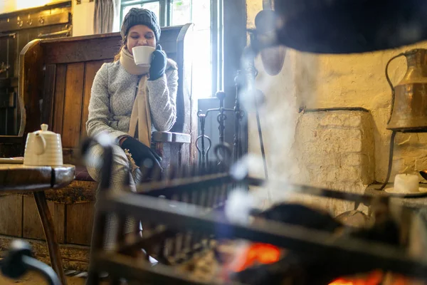 Joven hermosa mujer calentando con té junto a la chimenea — Foto de Stock