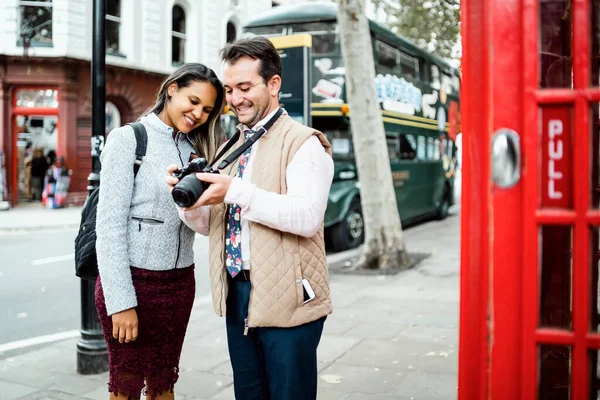 幸せな旅行のカップルは ロンドン 英国のカメラで写真をレビューします フレーム内のダブルデッキバスとレッド電話ブース — ストック写真