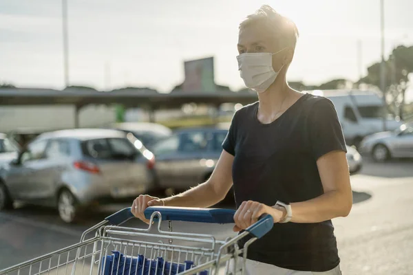スーパーマーケットの前でショッピングカートと保護顔マスクを身に着けている女性 — ストック写真