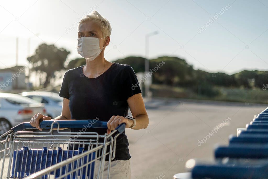 Woman wearing protective face mask with shopping cart in front of supermarket
