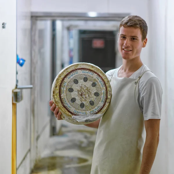 Trabalhador segurando uma roda de queijo no armazém — Fotografia de Stock