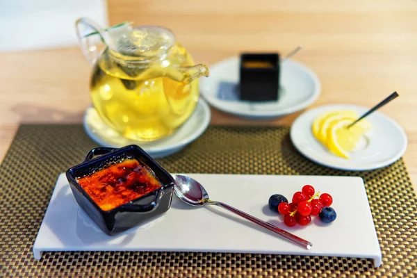 Creme caramel dessert served with fresh berries and teapot — Stock Photo, Image