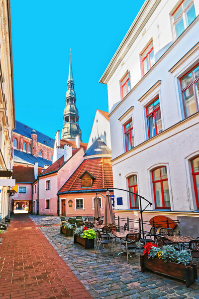 Street cafe and spire of St Peter Church in the historical center in the old town of Riga, Latvia.
