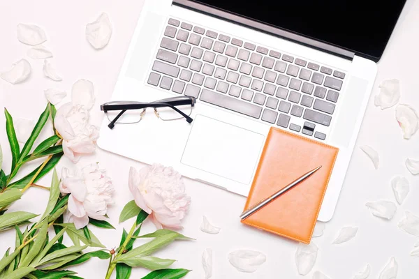 Workplace with laptop glasses notebook pen and peony flowers