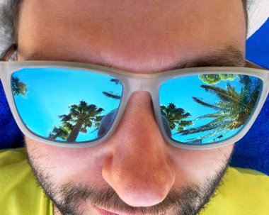 Tropikal palmiye ağaçları içinde güneş gözlüğü yansıyan