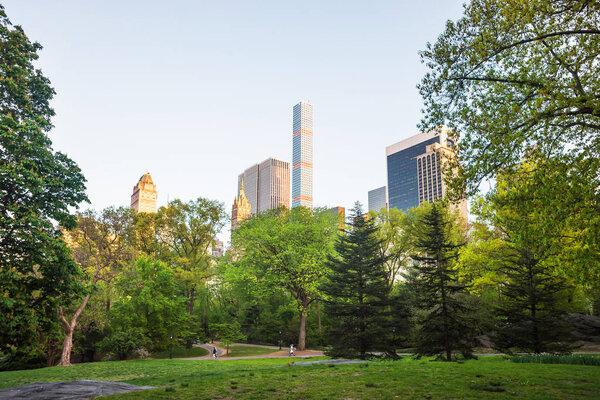 New York, USA - May 6, 2015: Green trees and Midtown Manhattan skyline viewed from Central Park South, in New York, NYC, USA. Tourists in the distance.