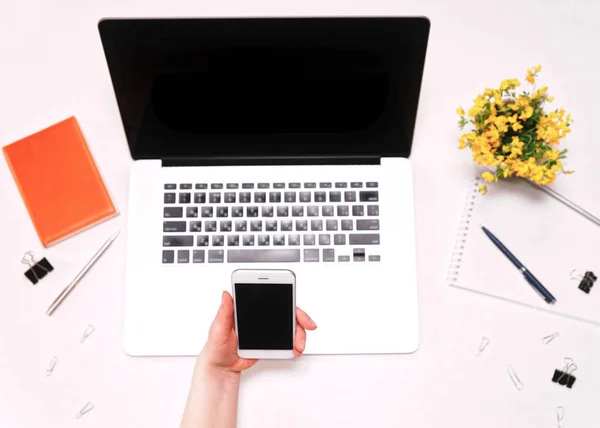 Pracovní prostor s ženou ruce drží telefon a notebook žluté květy — Stock fotografie