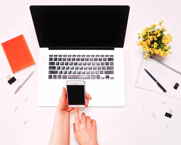 Pracovní prostor s ženské ruce drží telefon a notebook žluté květy — Stock fotografie