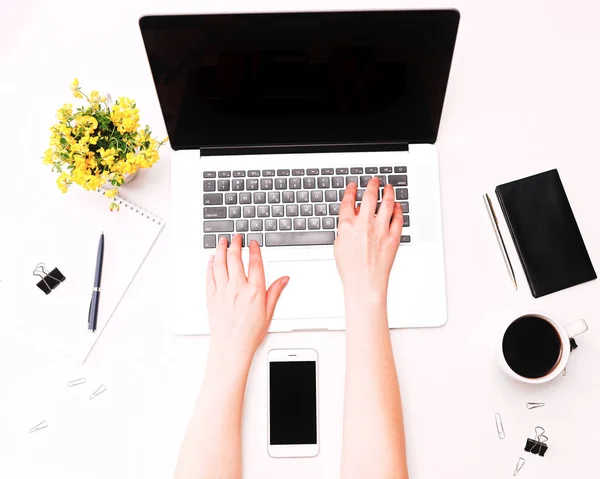 Espacio de trabajo con las manos de mujer en el teclado portátil flores de café móviles — Foto de Stock