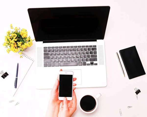 Espacio de trabajo con la mano de la mujer que sostiene el teléfono en el portátil flores amarillas — Foto de Stock