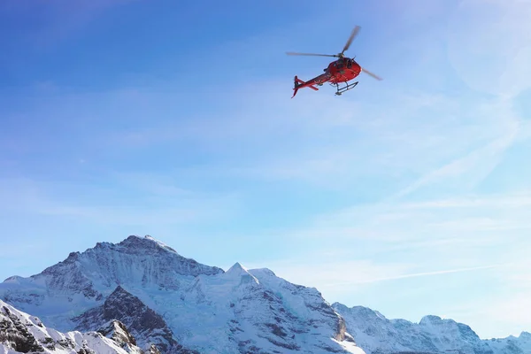 Helicóptero rojo volando en los Alpes suizos de montaña Mannlichen en winte —  Fotos de Stock