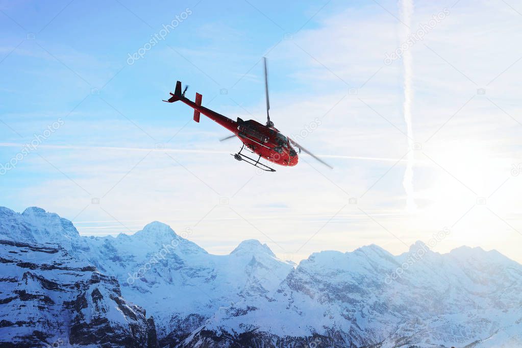 Red helicopter flying at Swiss Alps mountain Mannlichen winter s