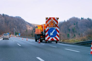 Sol yansıtıcı yol işaretinden aşağıya ok taşıyan bir kamyon.
