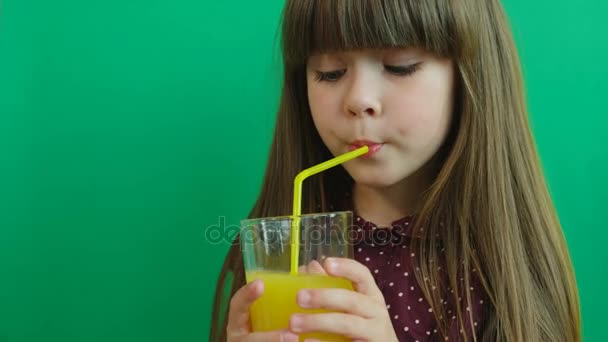 Bella ragazza liitle bere succo d'arancia con un colpo e sorridente alla fotocamera su sfondo verde parete. Chiudete. Ritratto — Video Stock