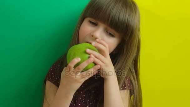 Söt liten flicka som försöker äta stora grönt äpple. Kid äta äpple. Gula och gröna bakgrunden. Rolig. Närbild — Stockvideo