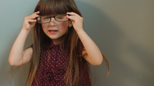 Konterfei eines süßen kleinen Mädchens, das eine Brille trägt und in die Kamera blickt. Nahaufnahme. grauer Hintergrund — Stockvideo