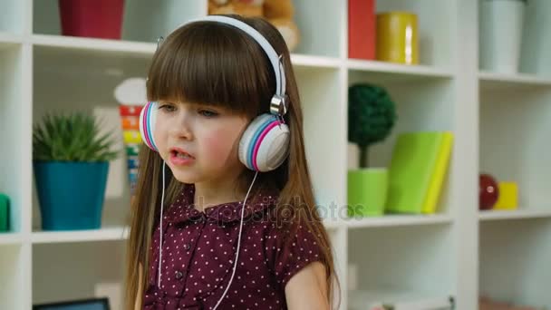 Linda niña cantando y bailando con auriculares en la habitación de los niños. Chica feliz bailando en casa — Vídeos de Stock