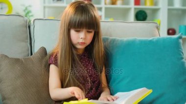 Güzel kız okuma kitabı ve düşünme, oturma odasında kanepede otururken penceresine bakarak. Yakın çekim