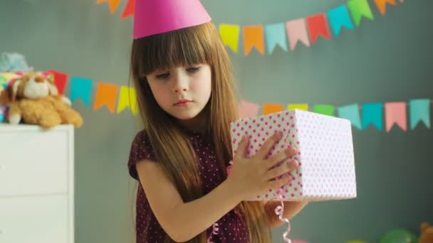 Gadis kecil yang lucu memegang dan berjabat kotak hadiah di tangan. Gadis kecil ingin tahu apa yang ada di dalam kotak. Tutup. — Stok Video
