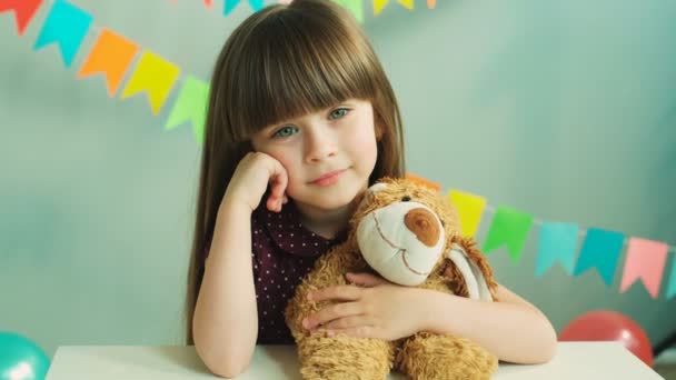 Retrato de una niña bonita abrazando a su osito de peluche en casa en la fiesta de cumpleaños. Chica sonriendo a la cámara — Vídeo de stock