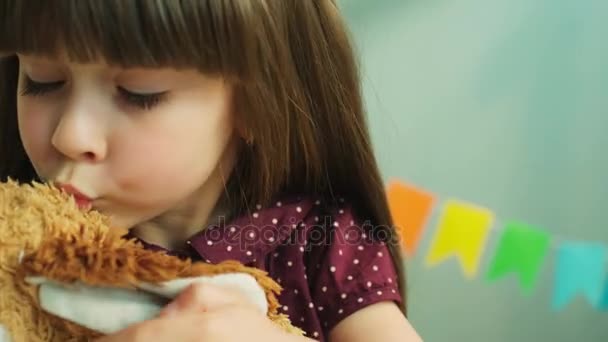 Linda niña besando su osito de peluche de juguete y mostrando la cadera a la cámara. De cerca. — Vídeos de Stock