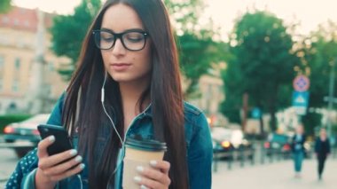 İletileri, Kentsel şehir sokak üzerinde yürürken kahve içme müzik yazarak akıllı telefon kullanarak güzel ve genç birbayan. Yakın çekim