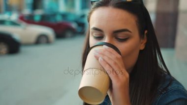 Kadın portre kadar kapatın. Çekici genç kadın kahve içme ve doğruca kameraya bakıyor. Şehir sokak arka plan