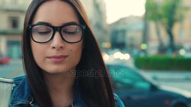 Retrato de mujer de cerca. Mujer morena atractiva en gafas mirando a la cámara y sonriendo en la calle. Ciudad calle tiro — Vídeos de Stock