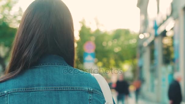 Beautiful young woman walking the city street and turning at the camera and smiling. Camera following behind. Slow motion — Stock Video