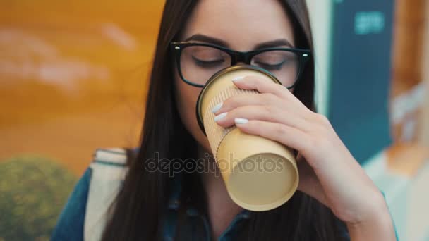 Retrato de mujer de cerca. Mujer atractiva en vasos bebiendo café y mirando directamente a la cámara y sonriendo. Ciudad calle ventanas fondo — Vídeo de stock