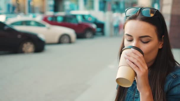 Mulher bonita olhando para a câmera sorrindo e bebendo café enquanto sentado nas escadas do lado de fora. Fechar — Vídeo de Stock