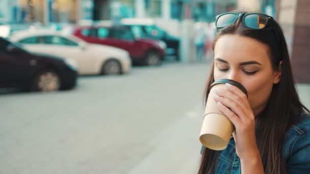 Hermosa mujer joven mirando a la cámara sonriendo y tomando café mientras está sentada en las escaleras afuera. De cerca. — Vídeos de Stock