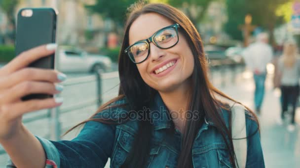 Joven hermosa mujer tomando selfies en el teléfono inteligente en la calle de la ciudad. Mujer posando en la cámara del teléfono inteligente, sonriendo. De cerca. — Vídeos de Stock