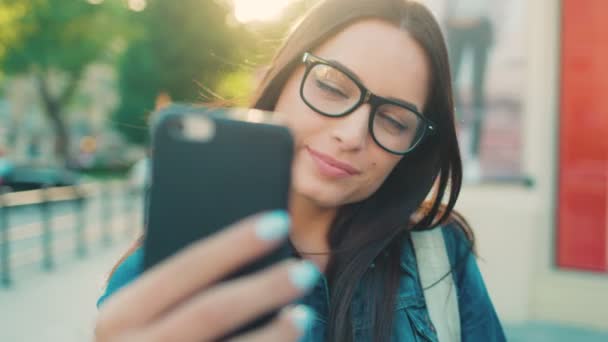 Acercamiento mujer atractiva joven tomando selfies en el teléfono inteligente en la calle de la ciudad. Mujer posando en la cámara del teléfono inteligente, sonriendo . — Vídeos de Stock