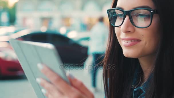 Acercamiento mujer atractiva en gafas usando tableta dispositivo de computadora fuera en la calle. Mujer sonriendo, tocando en la pantalla táctil, viendo videos, noticias . — Vídeos de Stock