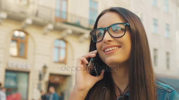 Glad ung kvinna jag glasögon talar på mobilen medan promenader på gatan. närbild — Stockvideo