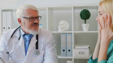 Beyaz orta doktor ofisinde oturan ve genç hasta baş ağrısı hakkında söyledim dinleme gözlüklü yaşlı. Kapalı.