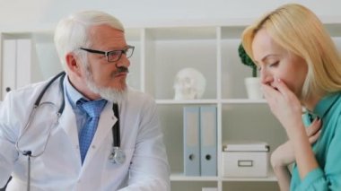 Öksürük hasta Bayan hasta için beyaz orta şikayet doktor boğazını hakkında ofiste oturan gözlüklü yaşlı.