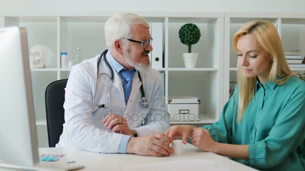 Médico varón de mediana edad caucásico en gafas, hablando de drogas y dando medicamentos a una paciente joven, sentado en el consultorio médico . — Vídeos de Stock