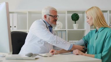 Kan basıncı beyaz genç güzel bayan hasta ölçme onun offise oturan beyaz ciddi erkek doktor. Kapalı.